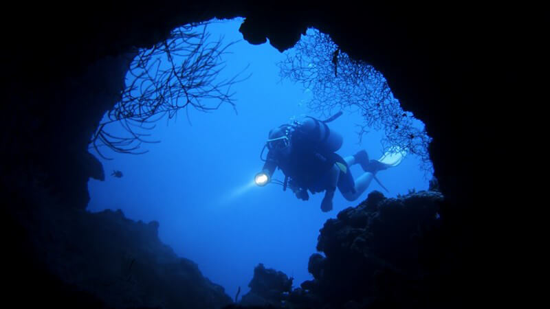 Taucher vor dunkler Höhle unter Wasser mit Taschenlampe, Foto aus Höhle geschossen