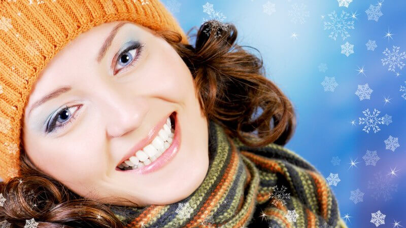 Junge dunkelhaarige Frau mit Wollmütze und Schal lacht in Kamera, im Hintergrund grafische Schneeflocken