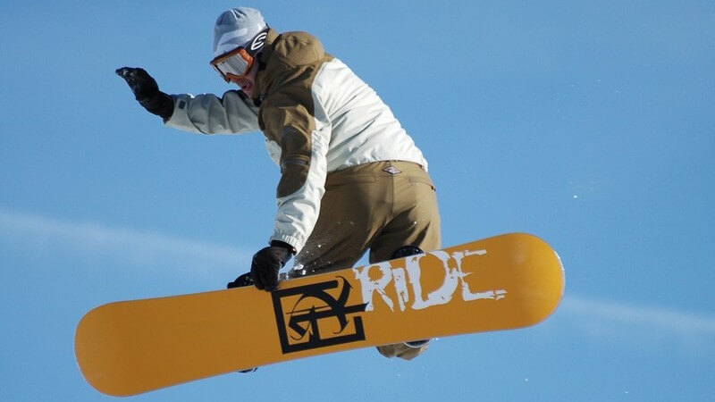 Snowboarder in der Luft vor blauem Himmel mit gelbem Snowboard