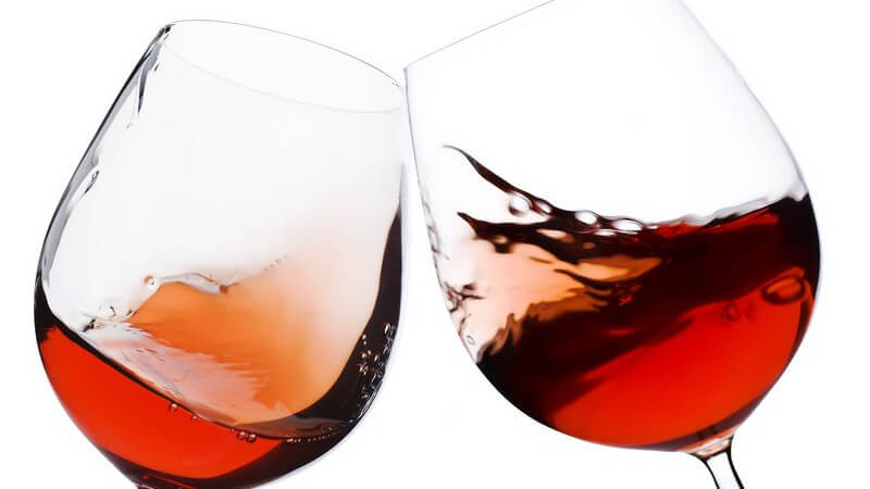 Nahaufnahme zwei Weingläser mit Rotwein beim Anstoßen
