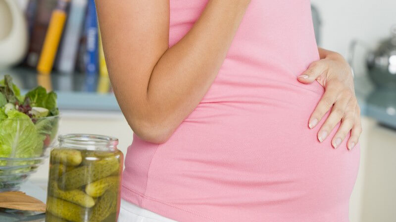 Schwangere Frau lächelt in Kamera und isst saure Gurken