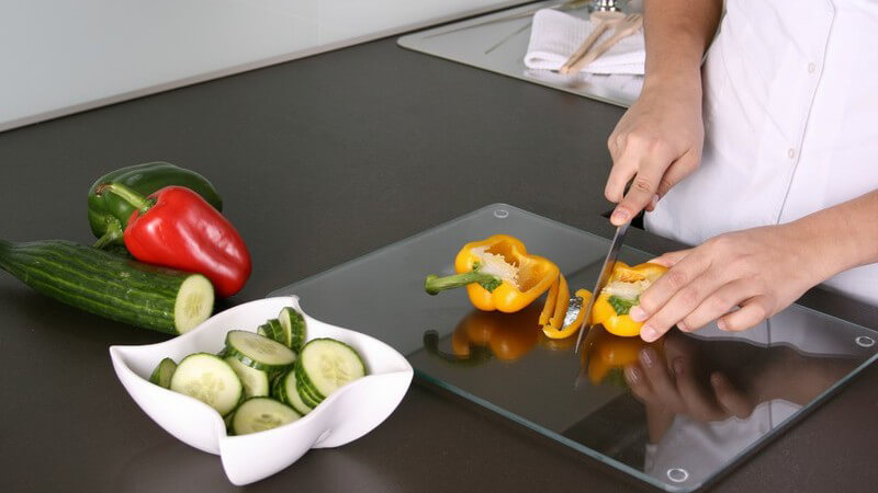 Frau in Küche schneidet Gemüse für Salat