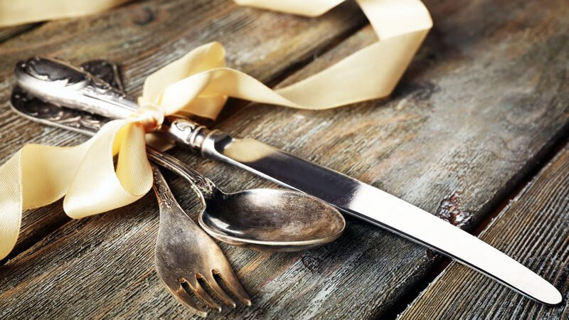 Altes Silberbesteck (Messer, Gabel und Löffel) zusammengebunden mit einer Schleife auf Holztisch
