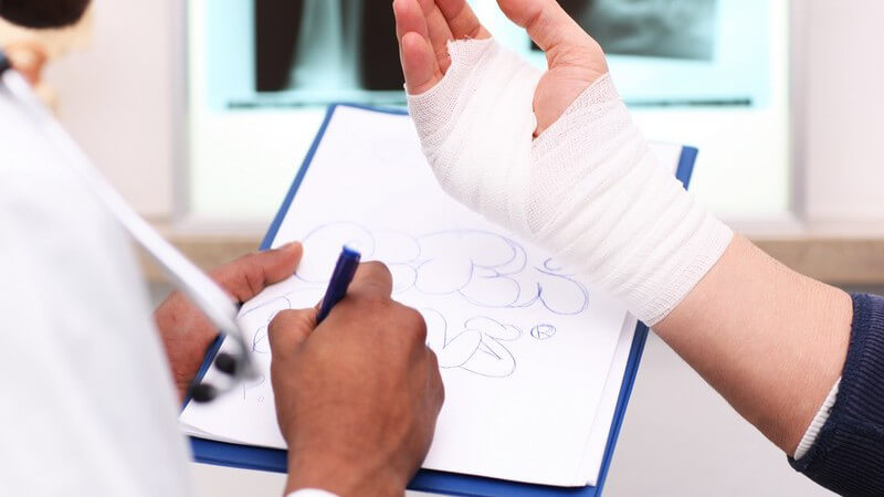 Bandagierte Hand mit Verband, im Hintergrund Röntgenbilder