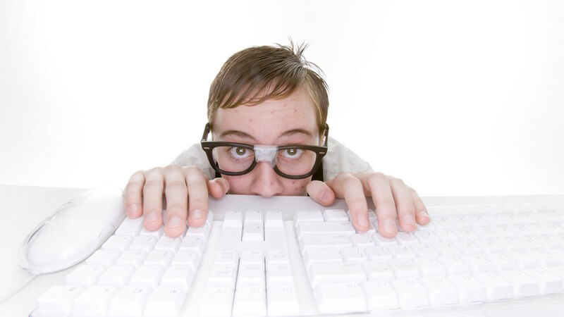 Schüchternder Computerfreak mit kaputter Brille sitzt an seiner Tastatur