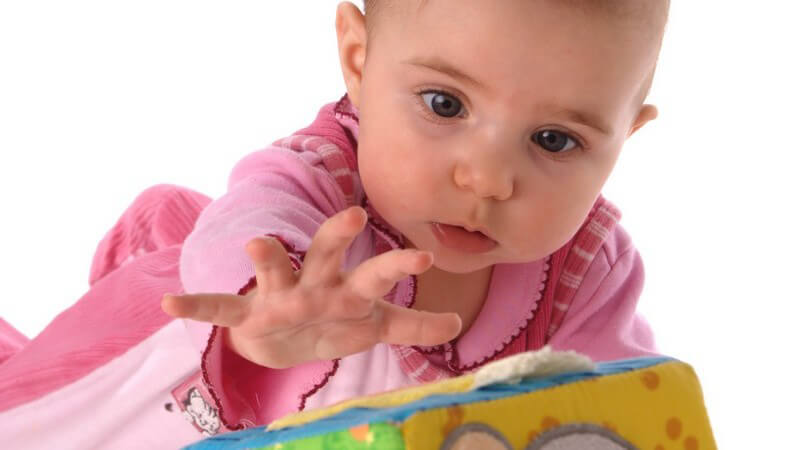 Baby krabbelt und greift nach Spielwürfel, weißer Hintergrund