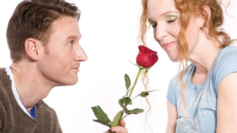 Er schenkt ihr eine rote Rose, sie riecht daran