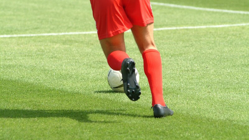 Beine eines Fußballers, läuft auf Fußballfeld hinter Ball her