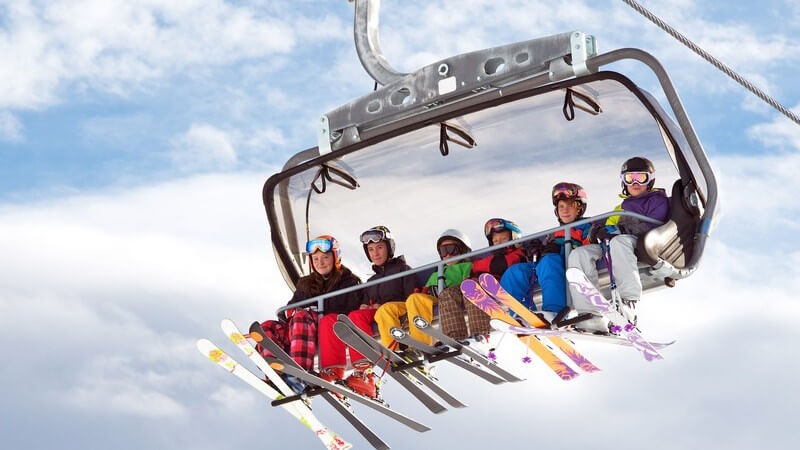 Mehrere Wintersportler mit Skiern sitzen im Sessellift