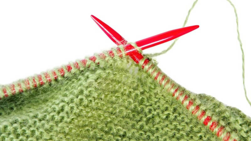Rote Stricknadeln mit grüner Wolle