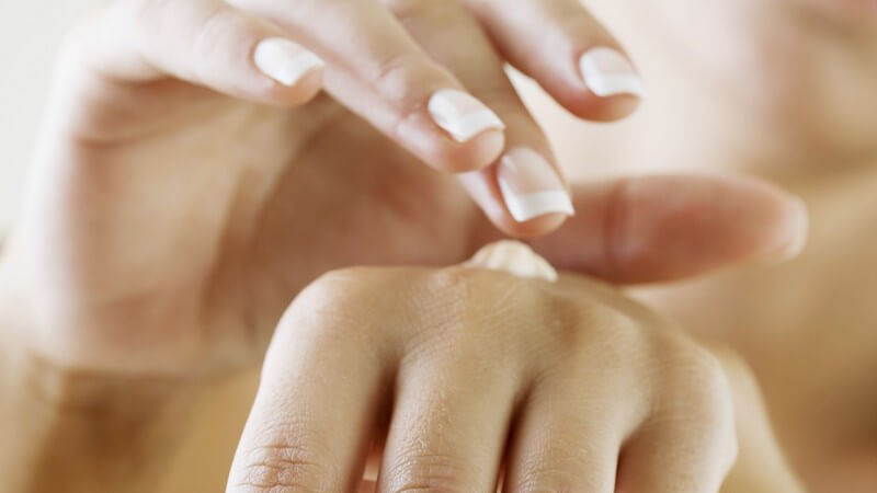 Frau mit French Nails Maniküre cremt sich die Hand mit Handcreme ein