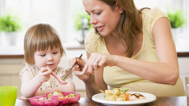 Schwangere Frau mit kleiner Tochter beim Essen