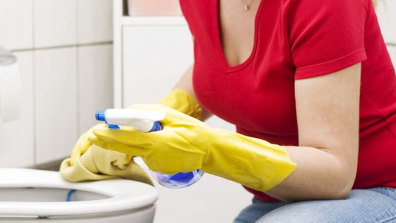 Junge Frau mit Handschuhen putzt Toilette, Badezimmer
