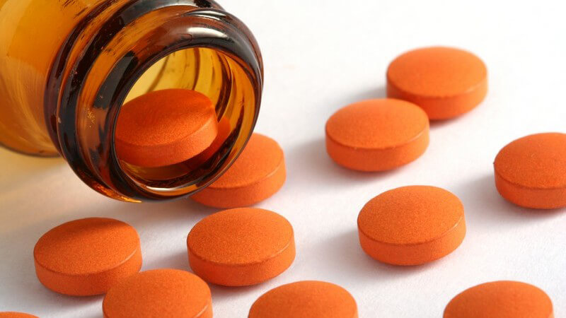 Orangene Tabletten aus brauner Glasflasche ausgekippt auf weißem Hintergrund
