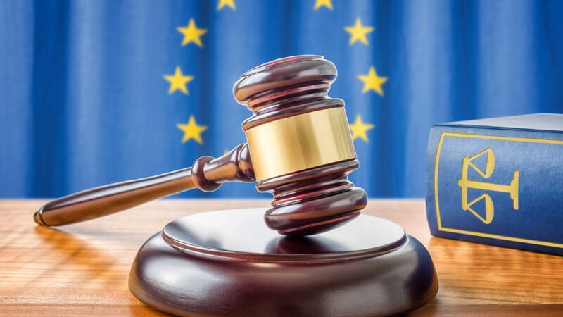 Richterhammer neben blauem Gesetzbuch vor der Flagge der Europäischen Union (EU)