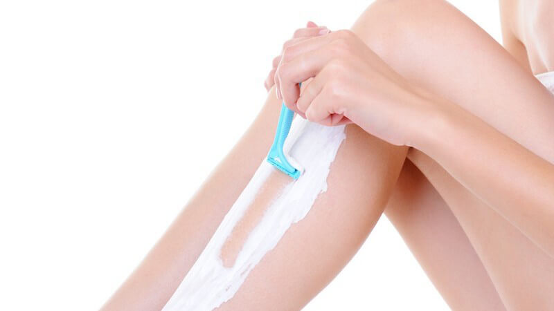 Frau rasiert sich die Beine mit Nassrasierer, weißer Hintergrund