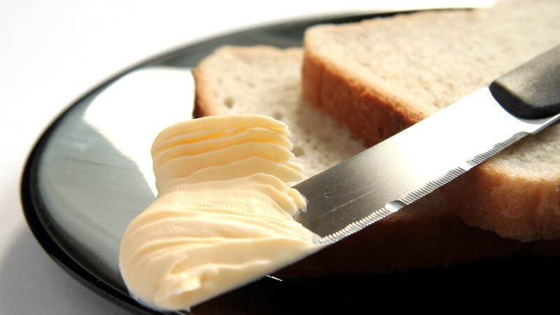 Nahaufnahme Brotscheiben auf schwarzem Teller, darauf Messer mit Butter