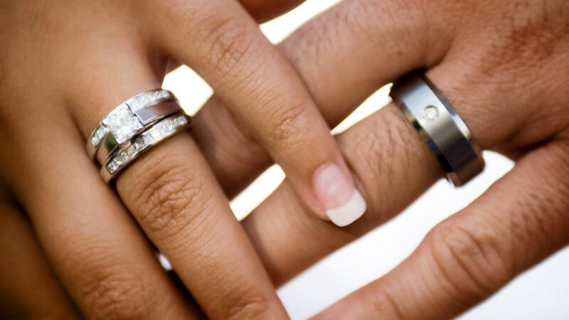 Frauenhand auf Männerhand, beide tragen Verlobungsring