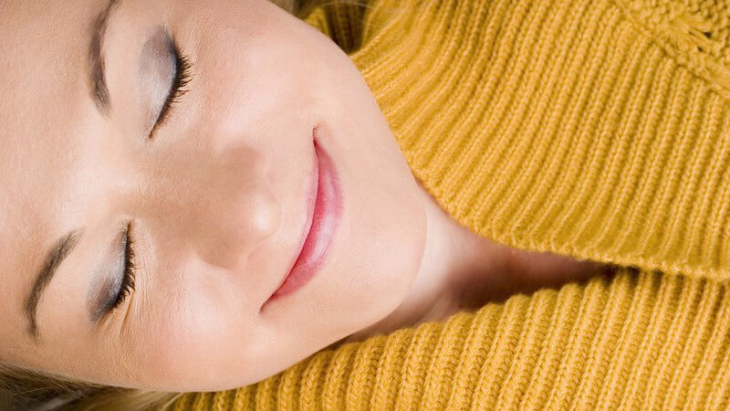 Frau in gelbem Strickpullover mit geschlossenen Augen und einem Lächeln