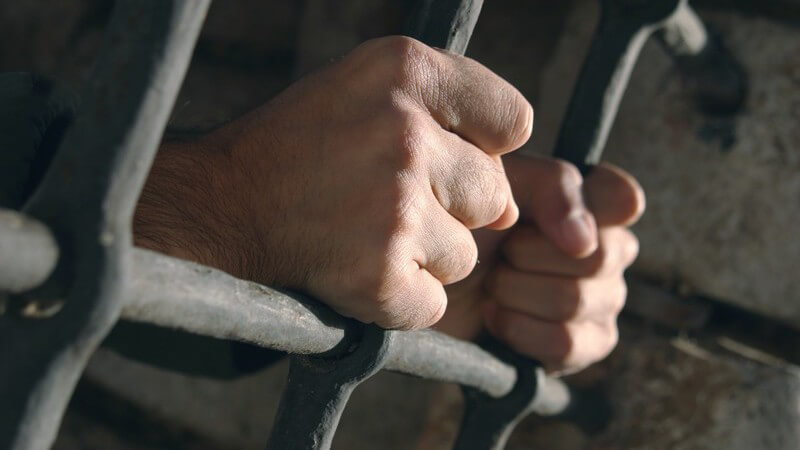 Hände eines Gefangenen halten sich an Gefängnis Gitter fest