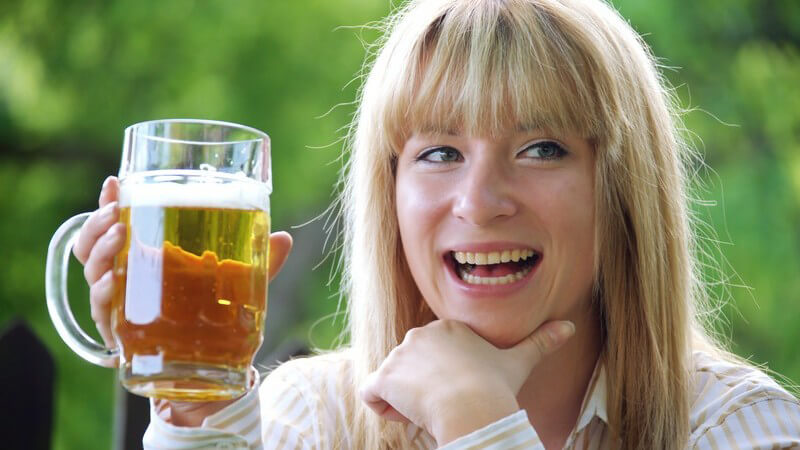 Junge lachende Frau hält Krug mit Bier nach oben