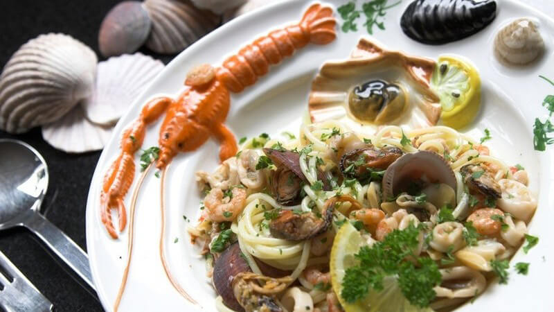 Gourmet Menü mit Meerestieren, Meeresfrüchten, Muscheln, auf Deko-Teller mit Muschel-Dekoration und Gabel und Löffel