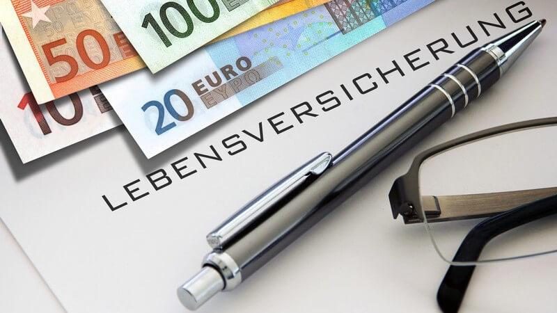Euro-Geldscheine, Kugelschreiber und Brille liegen auf einem Blatt mit der Aufschrift "Lebensversicherung"