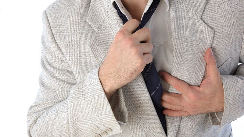 Mann im hellen Anzug löst sich mit der rechten Hand die dunkelblaue Krawatte und hält sich mit der linken den Brustkorb