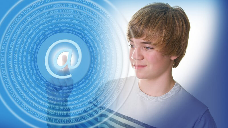 Jugendlicher vor blauem Hintergrund tippt mit dem Finger auf ein imaginäres E-Mail-Zeichen (@-Zeichen)