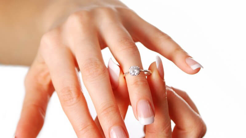 Frauenhände stecken Diamantring an, weißer Hintergrund
