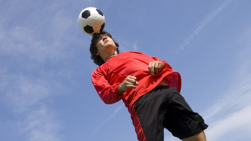 Dunkelhaariger Junge in Fußballkleidung springt und macht Kopfball