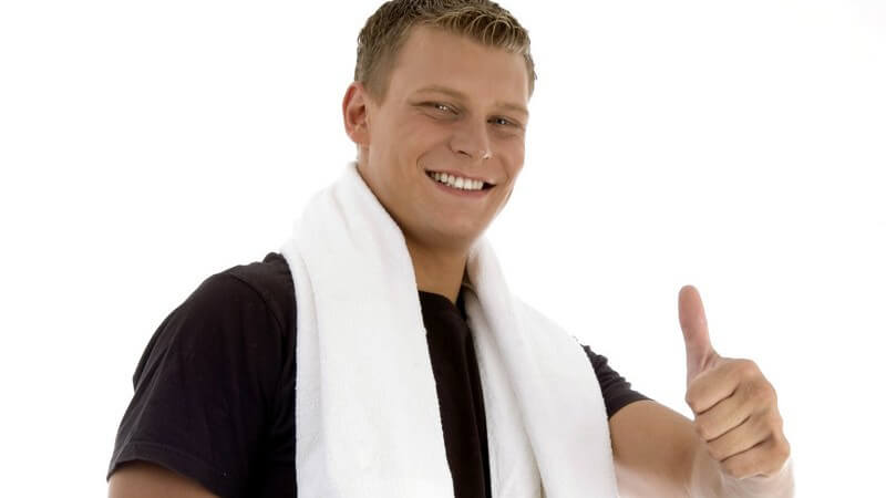 Sportlicher Mann mit schwarzem Shirt und weißem Handtuch zeigt den Daumen nach oben