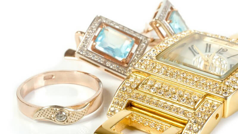 Goldschmuck auf weißem Hintergrund, Ring und Uhr mit Diamanten, zwei Ohrringe mit hellblauen Edelsteinen