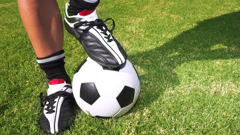 Füße eines Fußballers auf Wiese, ein Fuß auf Ball gestützt