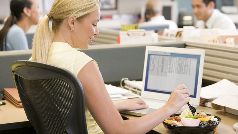 Junge Frau im Büro an ihrem PC isst Salat