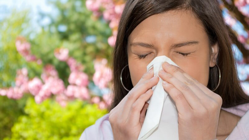 Junge Frau mit Allergie putzt sich die Nase