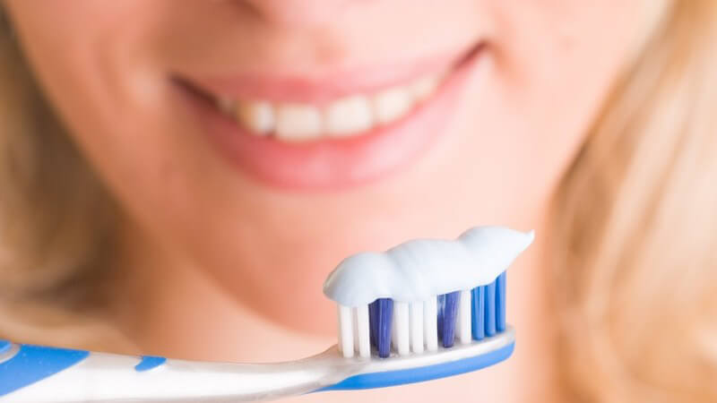 Zahnbürste mit Zahncreme, im Hintergrund Mund einer jungen Frau