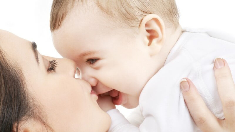 Junge Mutter hebt lachendes Baby hoch und küsst es auf die Nase