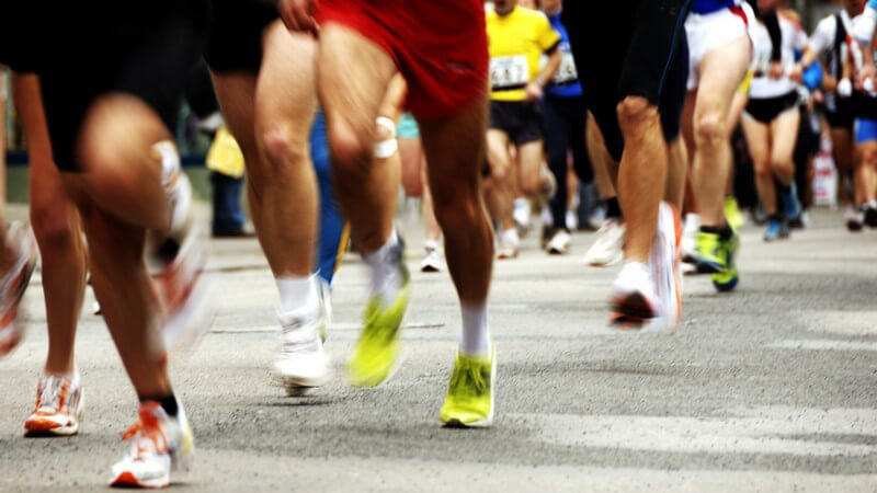 Beine und Füße von Marathonläufern auf grauem Asphalt