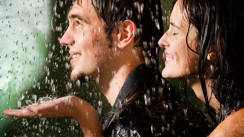 Junges glückliches Paar im Regen, sie umarmt ihn von hinten