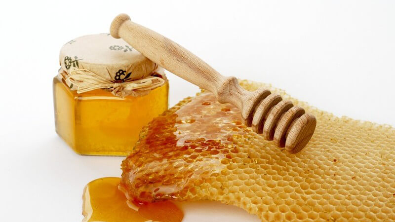Frischer Honig auf Waben neben Glas mit Honig und Honiglöffel