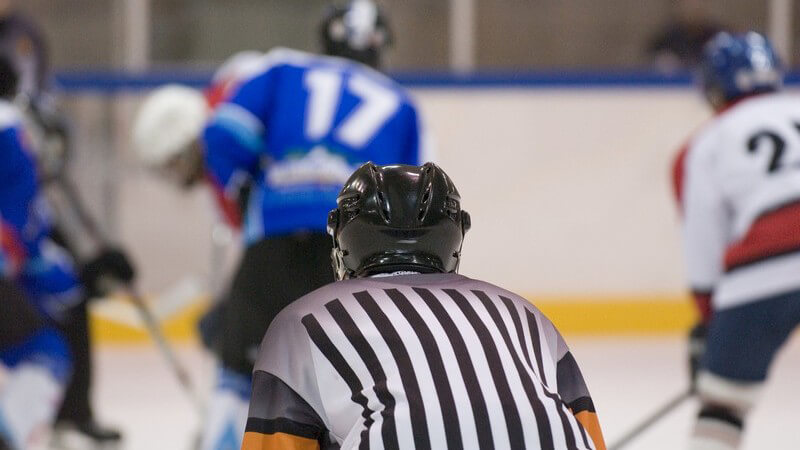 Eishockeyspiel - Schiedsrichter von hinten klar zu erkennen, mehrere Spieler unscharf auf dem Eis