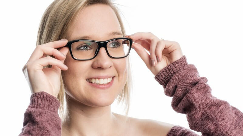 Junge blonde Frau probiert eine schwarze Hornbrille an
