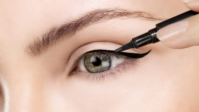 Frau zieht mit einem schwarzen Kajalstift eine schwarze Linie über ihrem linken Auge
