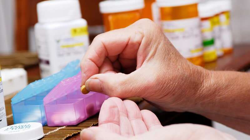 Seniorenhände legen Tabletten in verschiedene Behälter