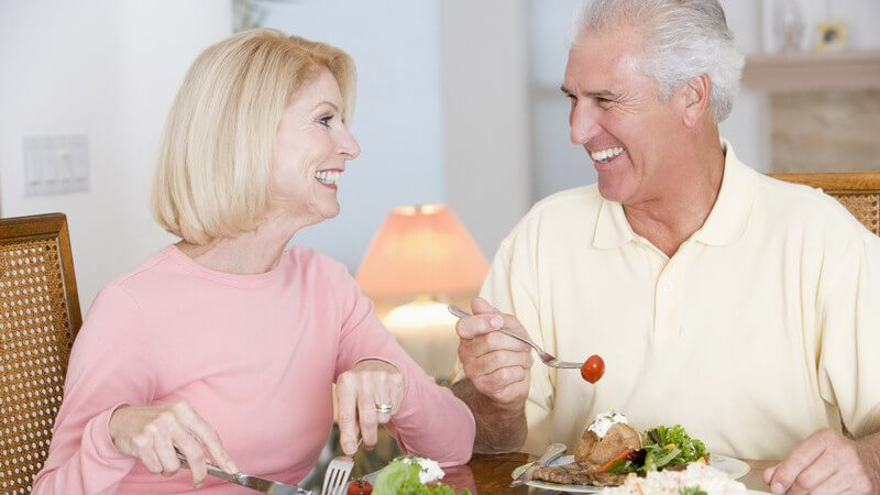 Älteres Paar beim Essen, schauen sich lachend in die Augen