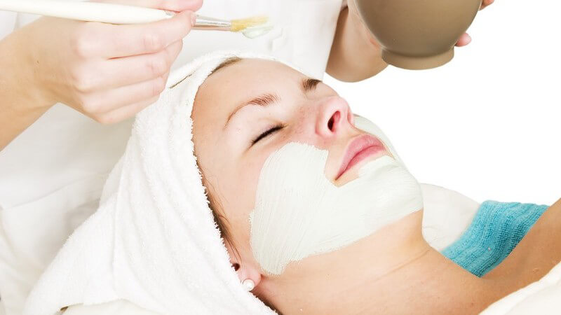 Gesichtspflege - Kosmetikerin trägt helle Gesichtsmaske auf