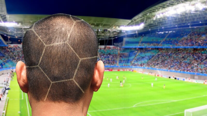 Braunhaariger Hinterkopf eines Mannes mit Fußballfrisur vor Fußballstadion