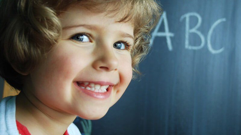 Kleines Mädchen in Klassenraum vor Tafel, darauf steht ABC