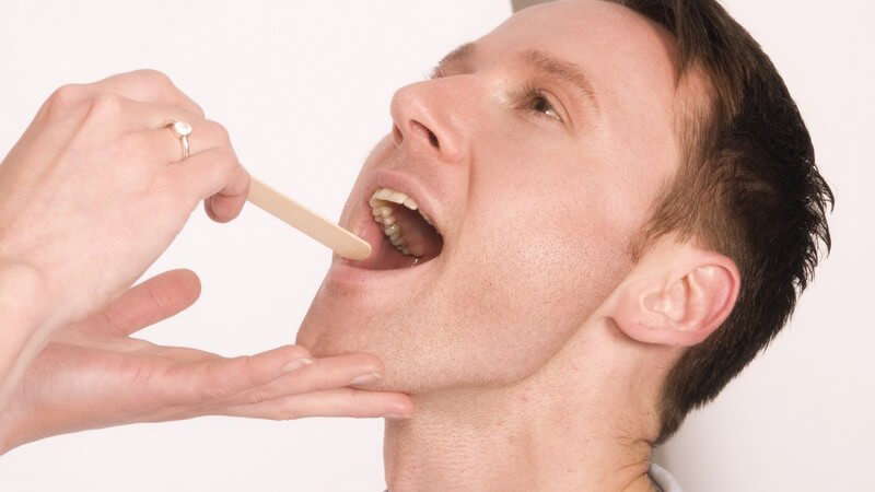 Untersuchung - Ärztin schaut einem Patienten mit einem Holzspatel in den Mund